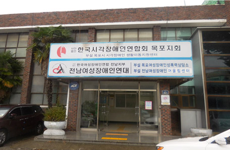 빨간 벽돌로 이루어진 건물에 한국시각장애인연합회 목포지회 부설 목포시 시각장애인 생활이동지원센터 라고 명시된 간판과 (사)한국여성장애인 전남지부 전남여성장애인연대 부설 목포여성장애인성폭력상담소 부설 전남여성장애인 어울림센터 라고 명시된 간판이 함께 걸려있는 모습