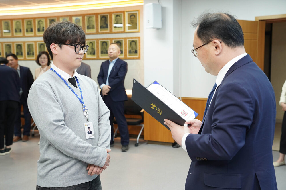 수시인사 임용장 수여식에서 정장을 입은 남성이 회색 맨투맨을 입은 안경 쓴 남성 직원에게 임용장을 전달하는 모습
