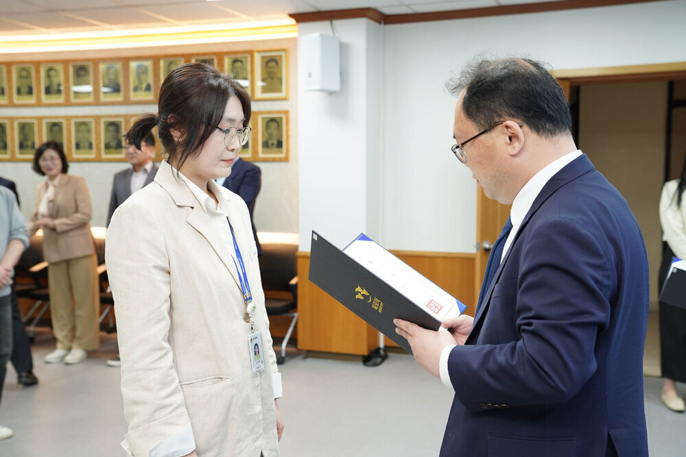 수시인사 임용장 수여식에서 정장을 입은 남성이 아이보리색 재킷을 입은 여성 직원에게 임용장을 전달하는 모습