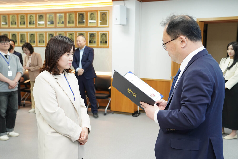 수시인사 임용장 수여식에서 정장을 입은 남성이 아이보리색 재킷을 입은 여성 직원에게 임용장을 전달하는 모습