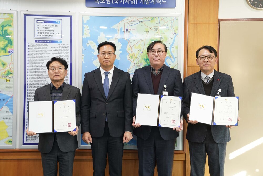 2026년 상반기 4급이하 정기인사로 정장을 입은 남성 세 명과 상장을 받은 남성 한 명이 실내 사무실 대형 지도 앞에서 기념 촬영을 하고 있으며, 양끝의 남성 두 명은 각각 펼쳐진 임용장을 양손으로 들고 정면을 응시하고 있다.