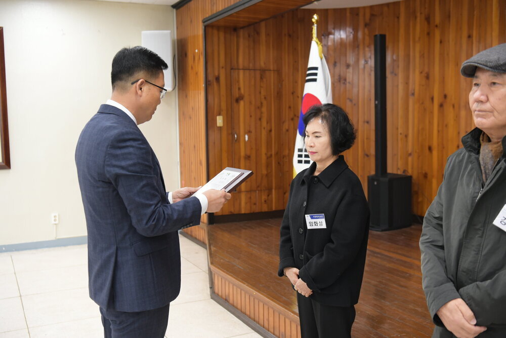 3월 정례조회에 정장을 입고 안경을 낀 남성이 위아래로 검은색 옷을 입은 임화성에게 패를 수여하고 있다.