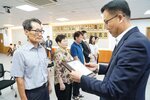 정장 차림의 관계자가 체크 셔츠를 입은 남성 수상자에게 표창패를 전달하며 내용을 읽고 있는 모습이다.
