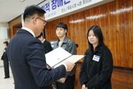 11월 정례조회로 정장을 입고 안경을 쓴 남성이 긴 단발머리에 검은색 코트를 입은 원민희 수상자에게 상장을 수여 하고 있다.